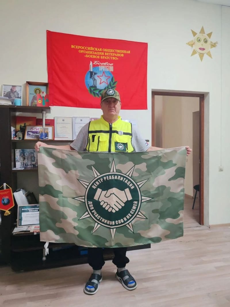 Юрий Николаевич Хлыбов держит флаг центра реабилитации